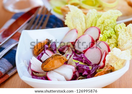Salad with radishes and mussels in white plate on wooden table.