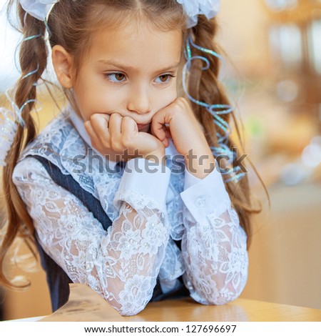 Little sad girl with beautiful bows sitting at wooden table.