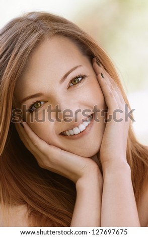 Portrait of smiling beautiful young woman with bare shoulders close up, against green of summer park.