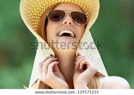 Portrait of beautiful smiling young woman in wide beach hat, against background of summer green park.