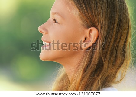 Portrait of young beautiful smiling girl in profile, against green summer garden.