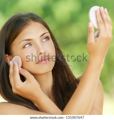 Beautiful young woman causes powder to skin, against summer green park.
