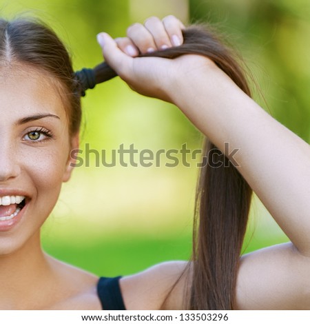 Beautiful dark-haired funny young woman holds up their tails, against background of summer green park.