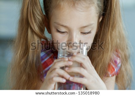 Portrait of beautiful little girl close-up, which sits on table and drinking water from glass.