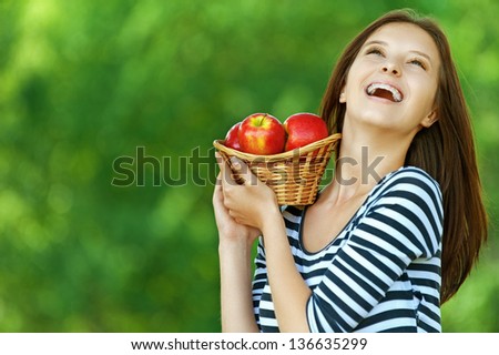 Young attractive woman holding basket with apples, against green of summer park.