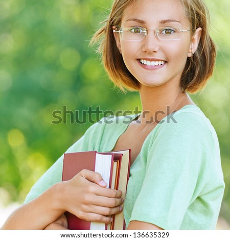 Portrait of smiling beautiful young woman-student with glasses, against background of summer green park.