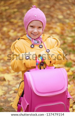 Beautiful smiling little girl in yellow coat with pink backpack goes to school.