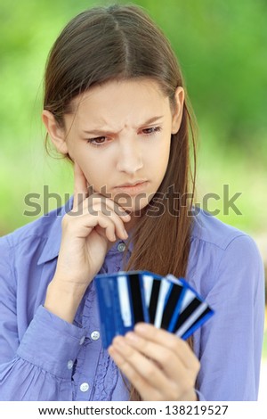 Sad teenage girl shows credit card, against green of summer park.