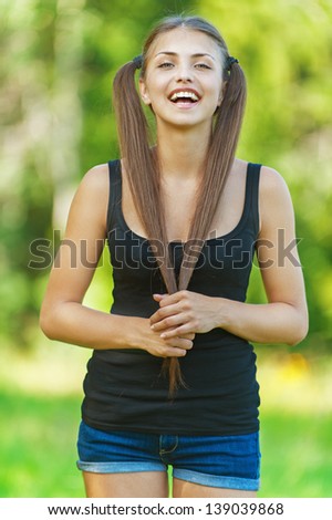 Portrait of an elegant, young, long-haired woman with two tails crossed them under the chin background summer green park