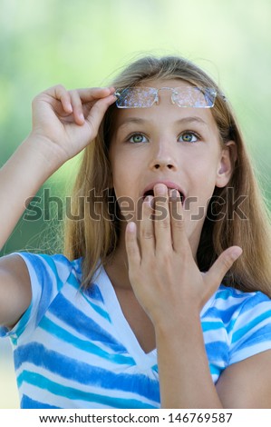 Beautiful teenage girl with her hand covers mouth in amazement, against green of summer park.