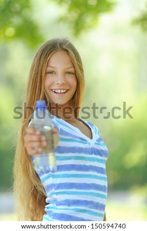 Beautiful teenage girl in blue blouse with water bottle, against green of summer park.