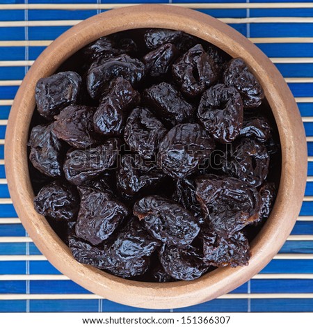 Dried prunes in wooden bowl on blue bamboo table cloth.
