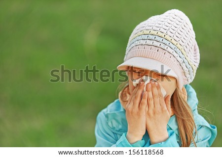 little girl in blue coat with handkerchief sneezes.