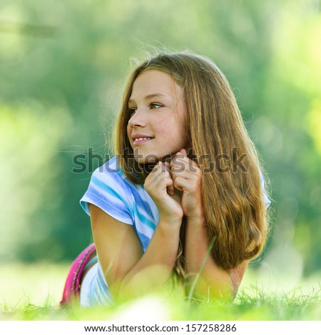 Beautiful smiling teenage girl in blue blouse lying on grass, against green of summer park.