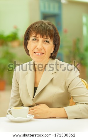Beautiful businesswoman in bright suit sitting at table drinking coffee.