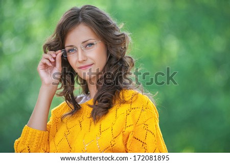 Portrait of pretty brunette young woman wearing eyeglasses and yellow blouse, standing at summer green park.