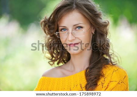 Portrait of pretty brunette young woman wearing eyeglasses and yellow blouse, standing at summer green park.