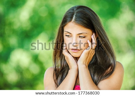 Portrait of young beautiful woman, who looks sadly down, on green background summer nature.