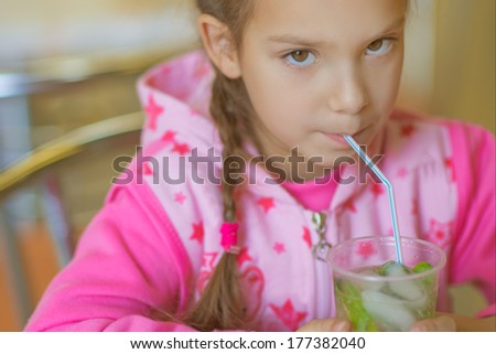 Little cheerful girl in pink jacket green juice drink .