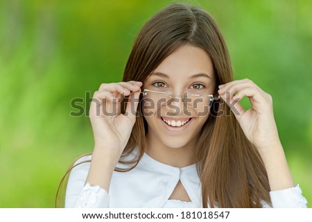 Portrait of pretty brunette young girl wearing eyeglasses and white blouse, standing at summer green park.