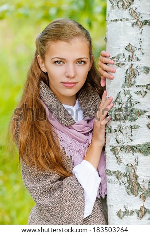 Portrait of sad beautiful young woman near birch, against background of autumn park.