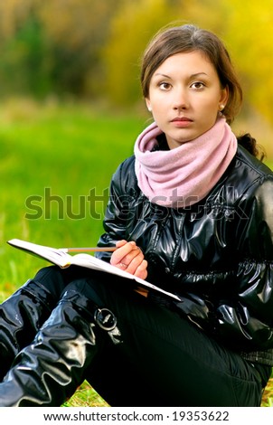 Young beautiful woman in black jacket reads book against autumn nature.