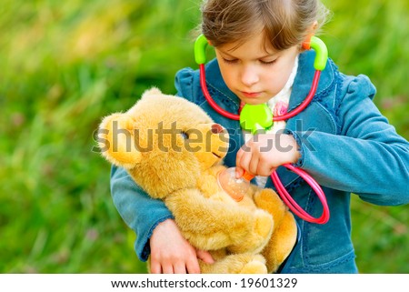 Small beautiful girl listens by means of stethoscope as heart of toy bear cub fights.