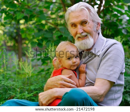 The grandfather sits on a lawn and holds the cheerful grand daughter on hands.