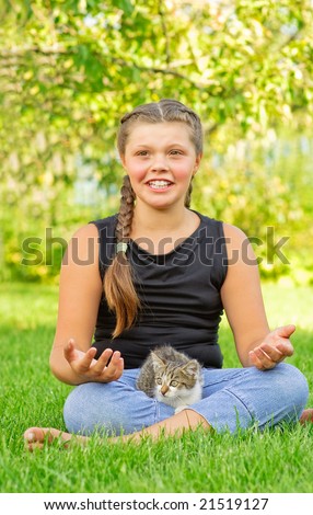 stock photo Young girl sits on green lawn with fluffy kitten at feet