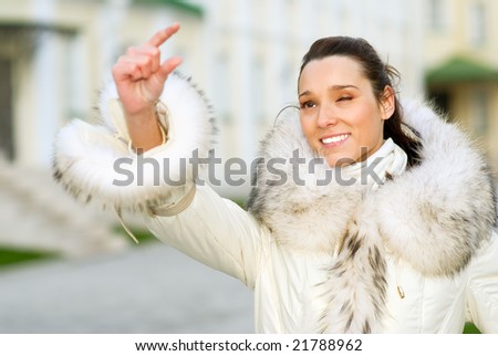 Girl measures in white fur coat by fingers lamppost height.