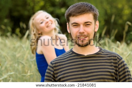 Young man with small beard laughs, and on background girl in a dark blue dress.
