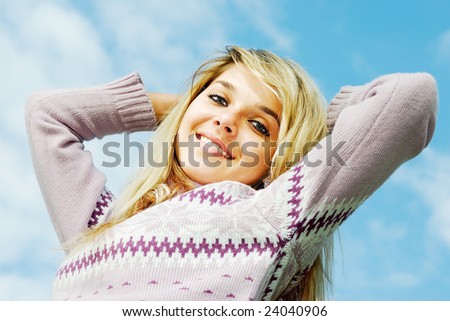 Young beautiful woman has rest, having combined hands behind  head, and smiles, against dark blue sky.