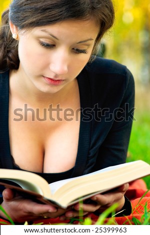Young beautiful woman in black jacket reads book against autumn nature.