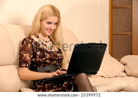 Young girl sits on sofa and works on laptop.