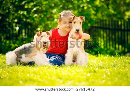 Little girl with two dogs of breed fox terrier on green lawn