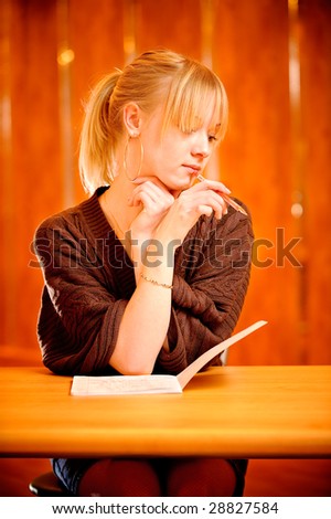 Fair-haired student sits at table and deliberates over right answer.