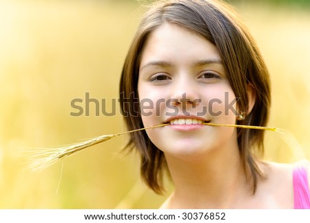 Young girl holds in teeth cone of rye against sowed field.