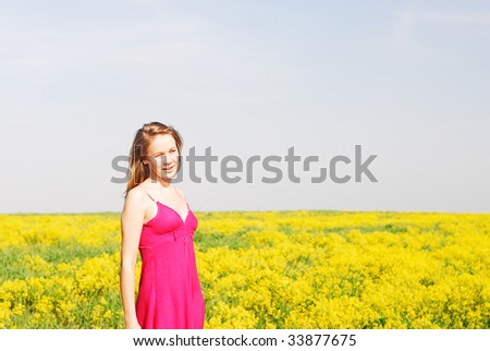 The young woman smiles and looks afar on a meadow where yellow flowers grow.