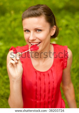Nice girl in red blouse eats sugar candy against summer nature.