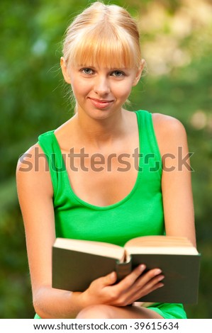 Nice girl-student reads textbook on history in city park.