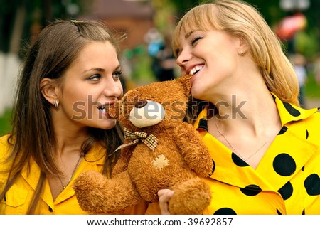 Two girls in yellow dresses tear teeth plush bear.