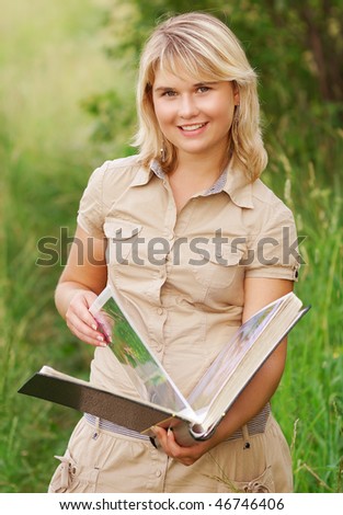 The beautiful young woman holds a picture album in hands and smiles, against a summer landscape.