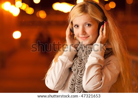 Beautiful girl in ear-phones in evening in city which is covered with fires.
