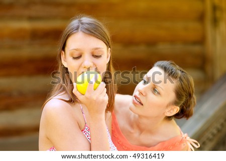 Beautiful young girl taking a bite of an apple. Other girl wishes to eat apple too.