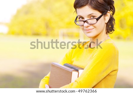 Young student holding books on autumn background.