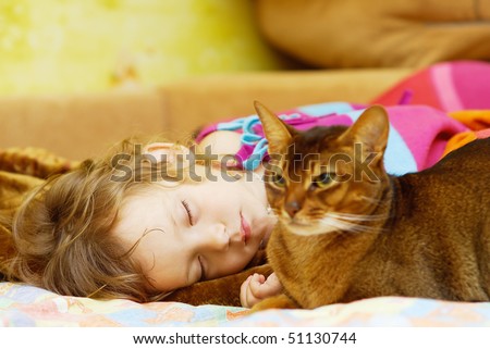 Little girl sleeps on bed, and near to it cat guards its rest.