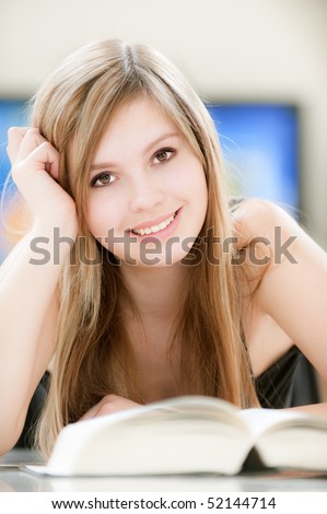 Smiling girl reads thick book against TV.