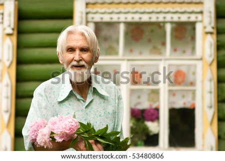 Elderly man with bouquet of fresh cut off peonies against personal plot.