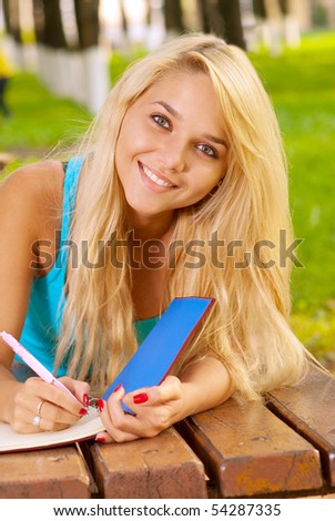 Girl-student in park writes in writing-book.
