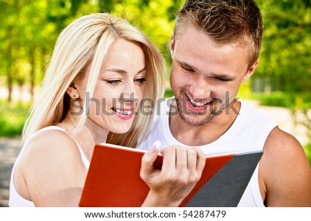 Two students read textbook against summer nature.